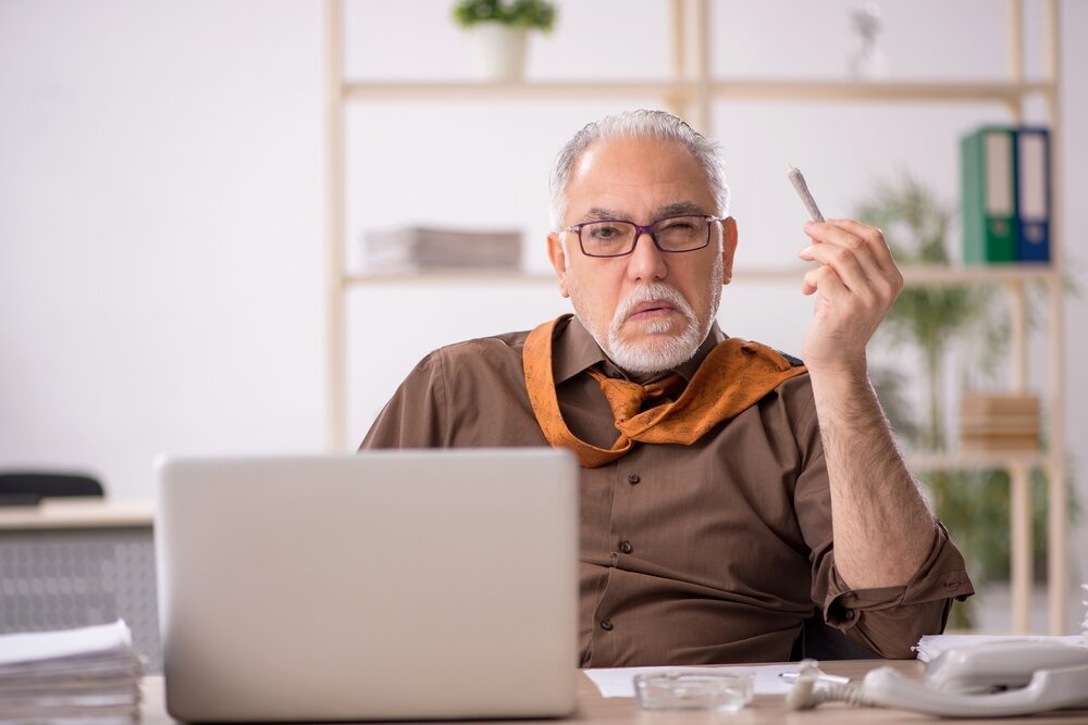 Cannabis in the Workplace. Old Male Employee Smoking joint at Workplace.